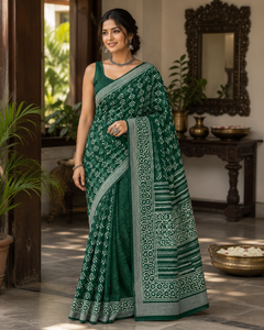 A woman wearing a dark green saree with intricate silver and white geometric patterns.