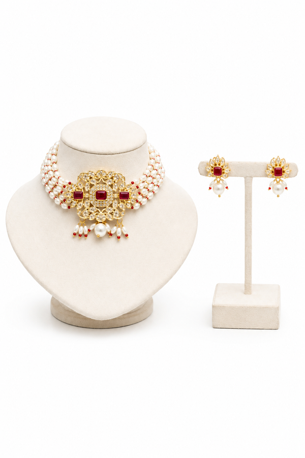 Gold-plated traditional Indian jewelry set featuring a choker necklace and matching stud earrings, embellished with white faux pearls and red stones, displayed on cream-colored jewelry.