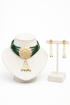 A gold and green beaded jewelry set displayed on a white stand, featuring a multi-strand necklace with a central gold floral motif and dangling pearl-like beads, alongside matching drop earrings.