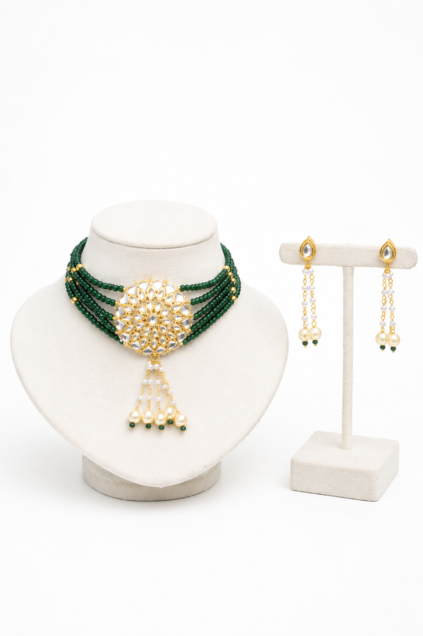 A gold and green beaded jewelry set displayed on a white stand, featuring a multi-strand necklace with a central gold floral motif and dangling pearl-like beads, alongside matching drop earrings.