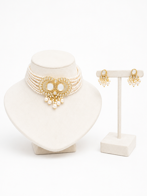 A gold and pearl jewelry, featuring a multi-strand choker necklace with a central ornate gold medallion and dangling pearls, alongside matching drop earrings.