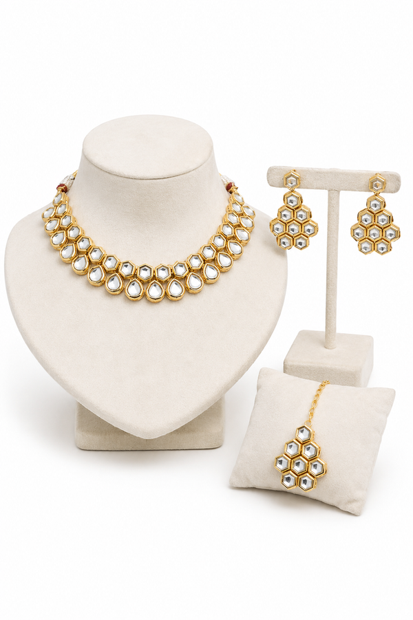 Gold-plated jewelry set featuring a multi-strand pearl necklace on a cream display bust, matching floral drop earrings and a matching forehead tikka on a small cushion.