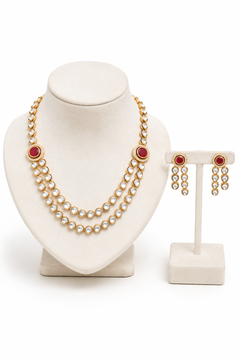 Gold-plated double-strand pearl necklace set with oval red gemstone accents, alongside matching drop earrings on a stand.