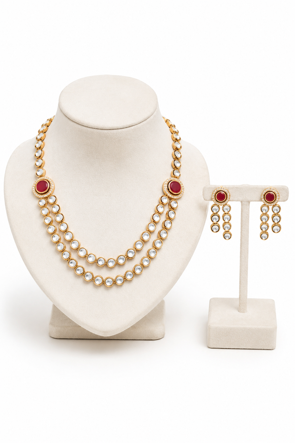 Gold-plated double-strand pearl necklace set with oval red gemstone accents, alongside matching drop earrings on a stand.