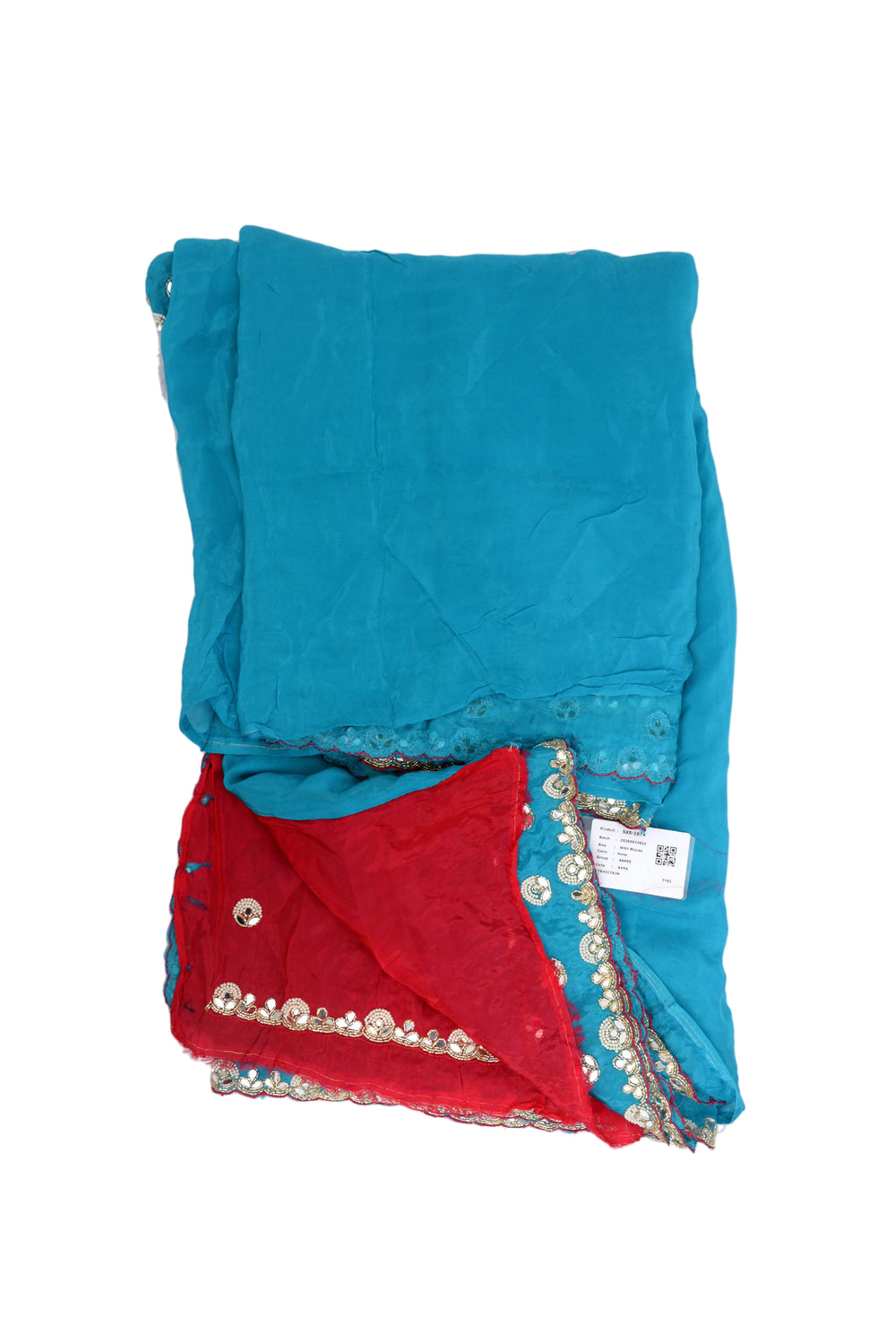 A woman modeling a turquoise blue saree with a red sleeve blouse, decorated with gold and silver mirror work borders and floral embroidery, set against a textured beige studio backdrop.