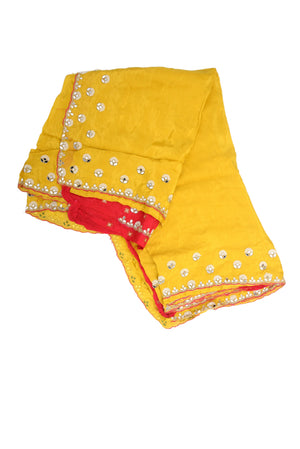 A folded yellow fabric garment, likely a traditional skirt or dupatta, decorated with silver mirror work and a red inner lining, shown on a plain white background.