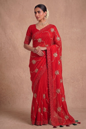 A woman modeling a bright red georgette saree with gold floral embroidery and a matching red embroidered blouse.