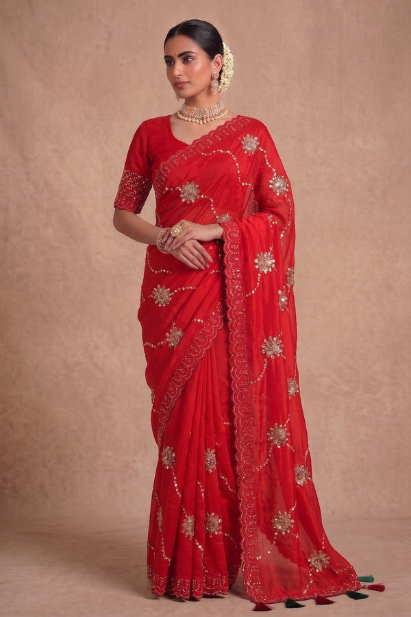 A woman modeling a bright red georgette saree with gold floral embroidery and a matching red embroidered blouse.