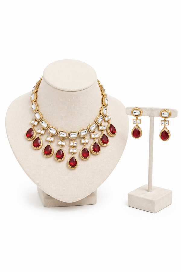 Gold-plated jewelry set featuring a statement necklace and matching drop earrings with red teardrop gemstones and white pearl-like accents.