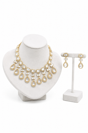 Gold-toned jewelry set featuring a statement necklace on a white bust display and matching drop earrings on a white stand.
