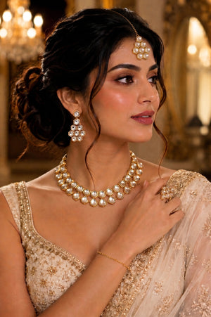 A woman wearing a traditional Indian outfit with gold embroidery, styled with a pearl necklace, matching pearl earrings, a maang tikka.