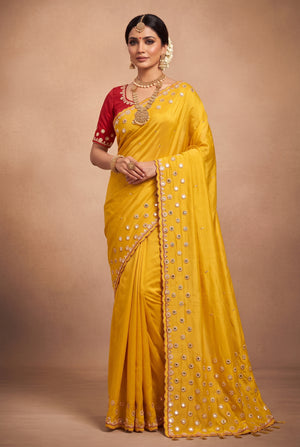 A woman modeling a bright yellow saree with silver mirror work embroidery and a contrasting red blouse.