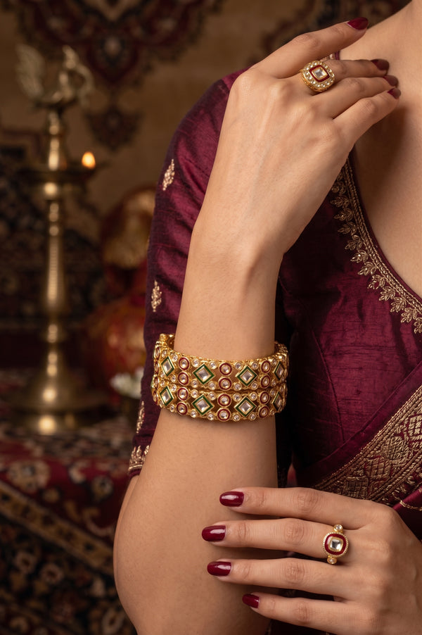 A close-up of a woman wearing a wide gold-plated bangle bracelet with green and red stones.
