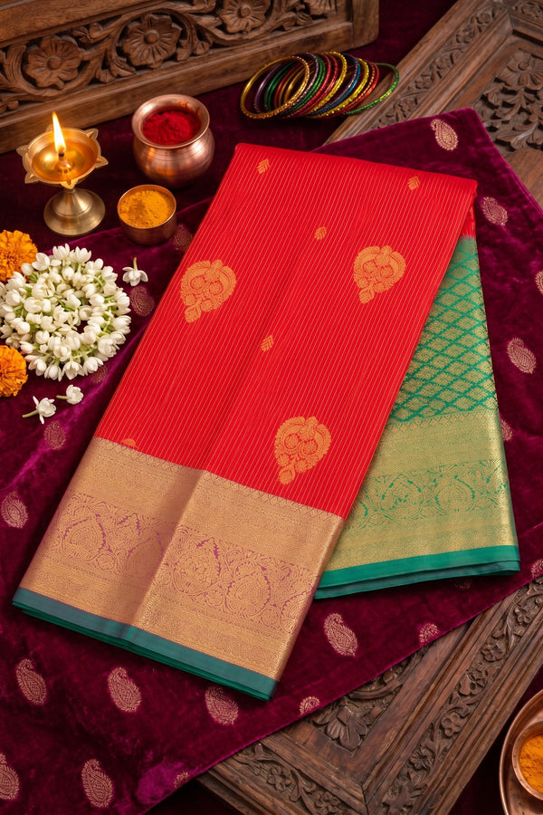 A folded red and green silk saree with gold zari motifs and a beige border.