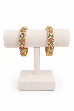 A pair of gold-plated bangles decorated with green, red, and white stones.