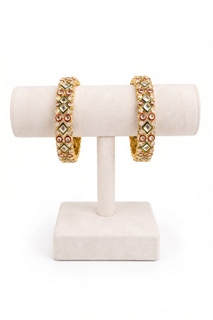 A pair of gold-plated bangles decorated with green, red, and white stones.