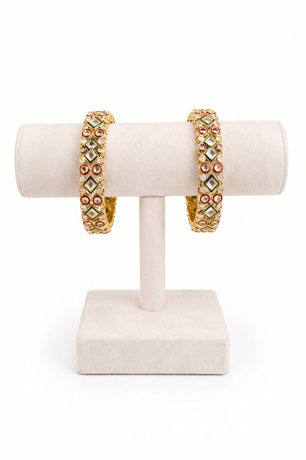 A pair of gold-plated bangles decorated with green, red, and white stones.
