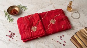 A folded red saree with gold embroidered floral motifs and scalloped edges.