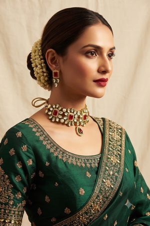 A woman wearing a Gold and white & Ruby red stone jewelry set featuring a choker necklace and matching drop earrings.